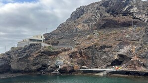 A rocky coastline with a clear water body, a bridge, and a building on the hill. - El Rinconcito Home in Tamaduste 5 Min from Beach (Tamaduste)