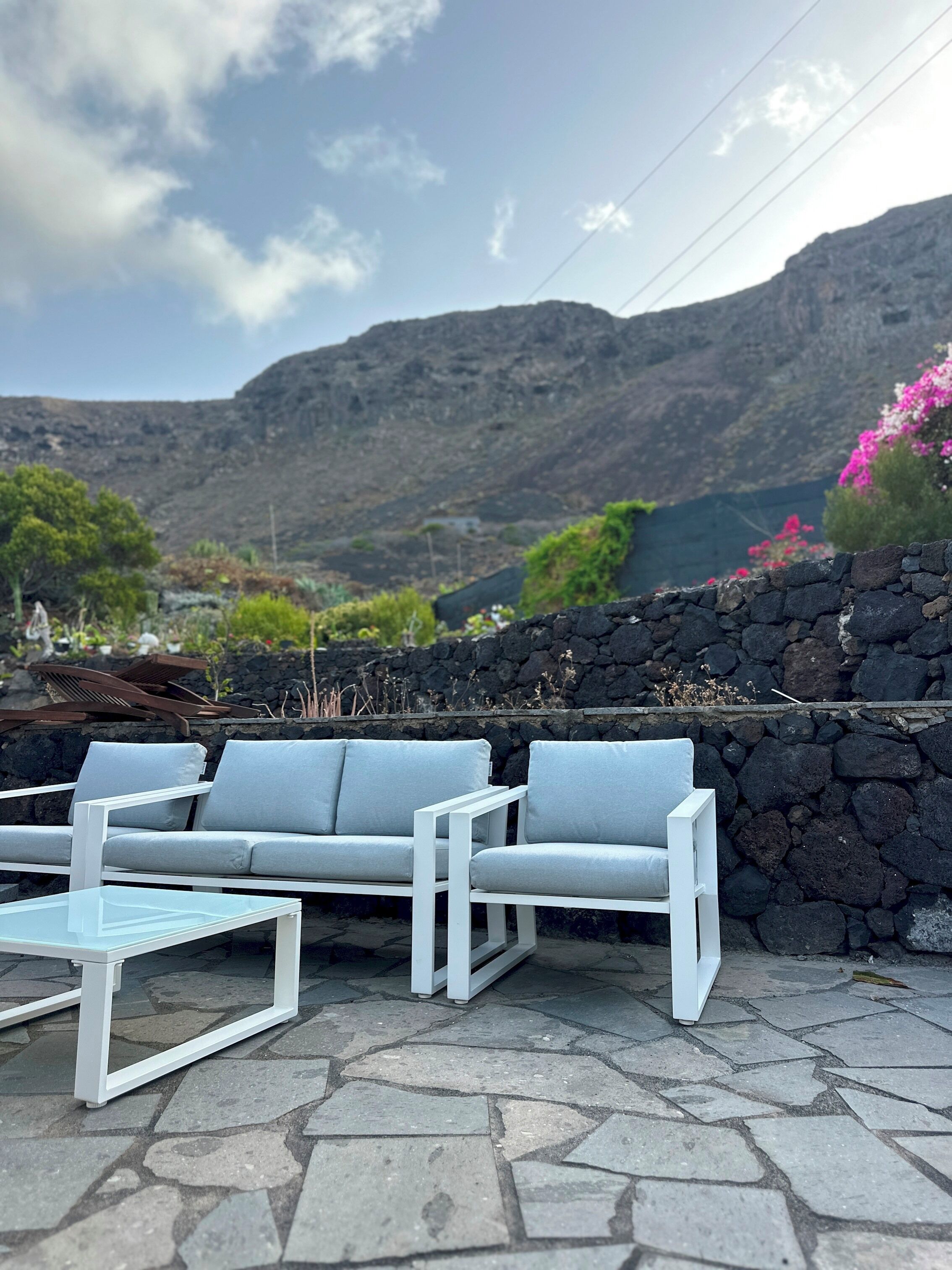 Una zona de estar con una mesa y sillas blancas, una pared de piedra y un paisaje montañoso al fondo.