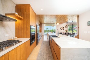 A modern kitchen with a central island, wooden cabinetry, and a view to a dining area. - Exclusive 4-Villa Beach Estate 11 BR • Sleeps 22 (Pinilla)
