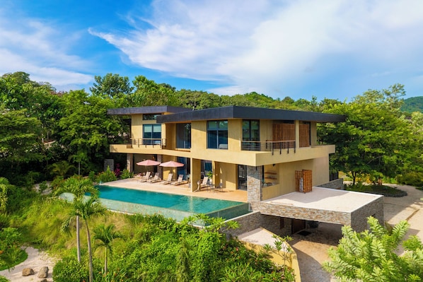 Uma casa moderna de dois andares com piscina, rodeada por vegetação exuberante.