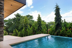 A swimming pool with a wooden deck and a stone wall, surrounded by lush greenery and trees. - Exclusive 4-Villa Beach Estate 11 BR • Sleeps 22 (Pinilla)