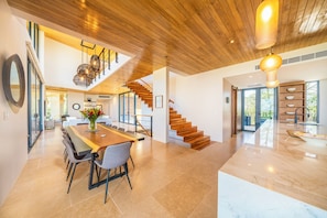 Uma cozinha ampla com uma ilha grande, uma área de jantar com uma mesa comprida e uma escadaria que leva a um andar superior.