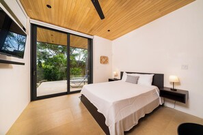 A bedroom with a bed, bedside tables, a TV, and a sliding glass door leading to an outdoor area. - Exclusive 4-Villa Beach Estate 11 BR • Sleeps 22 (Pinilla)