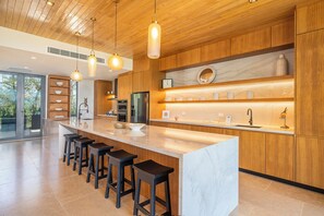 A modern kitchen with a central island, bar stools, wooden cabinetry, and pendant lighting. - Exclusive 4-Villa Beach Estate 11 BR • Sleeps 22 (Pinilla)