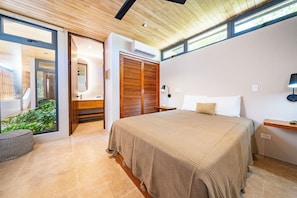 Quarto moderno com uma cama grande, uma mesa de cabeceira e uma luminária na parede.