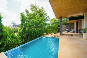 Une piscine dotée d’une terrasse en bois et de chaises longues, entourée d’une végétation luxuriante.