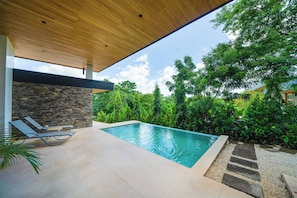A modern outdoor pool area with a stone wall, lounge chairs, and a wooden ceiling. - Exclusive 4-Villa Beach Estate 11 BR • Sleeps 22 (Pinilla)