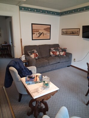 Ein Wohnzimmer mit einer Couch, einem Couchtisch mit Büchern und einer dekorativen Vase, sowie zwei gerahmten Bildern an der Wand.