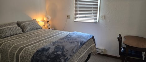 Un dormitorio con cama, lámpara de noche y ventana con persianas.