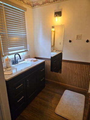 Baño con lavamanos, espejo, tocador y piso de madera.