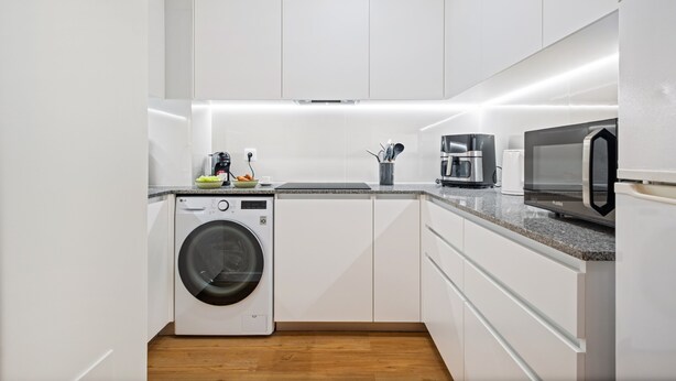 Een moderne keuken met witte kastjes, een wasmachine, een koffiezetapparaat en een magnetron.