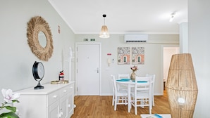 Een moderne kamer met een witte inloopkast, een spiegel, een brandblusser, een eettafel met stoelen, een hanglamp en een wandairconditioner.