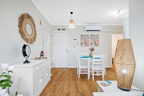 A modern room with a white wardrobe, a mirror, a fire extinguisher, a dining table with chairs, a hanging light fixture, and a wall-mounted air conditioner. - Imperatriz 2D by Homie (Funchal)