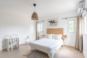 Ein Schlafzimmer mit einem Bett, einem Sessel, einem Nachttisch, einer Pendelleuchte, einem Fenster und einer Wand-Klimaanlage.