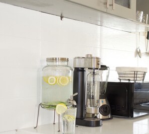 Een aanrecht met een grote glazen pot, een blender en een glas water met citroenpartjes.