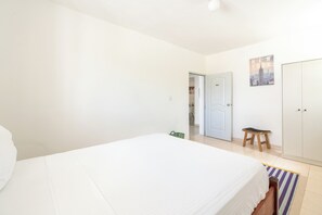 A bedroom with a bed, a wardrobe, a door leading to another room, and a small stool. - Apartment with Private Garden and BBQ Area (La Romana)
