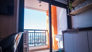 Un balcón con vista a la ciudad, una ventana con persianas y un pequeño contenedor de basura.