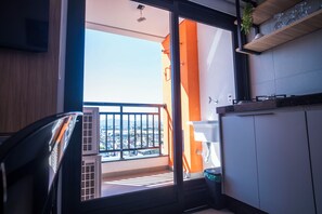 Un balcón con vista a la ciudad, una ventana con persianas y un pequeño contenedor de basura.