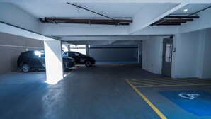 A parking garage with two cars parked, a blue handicap parking space, and a door on the right. - Vista Cecap (Guarulhos)