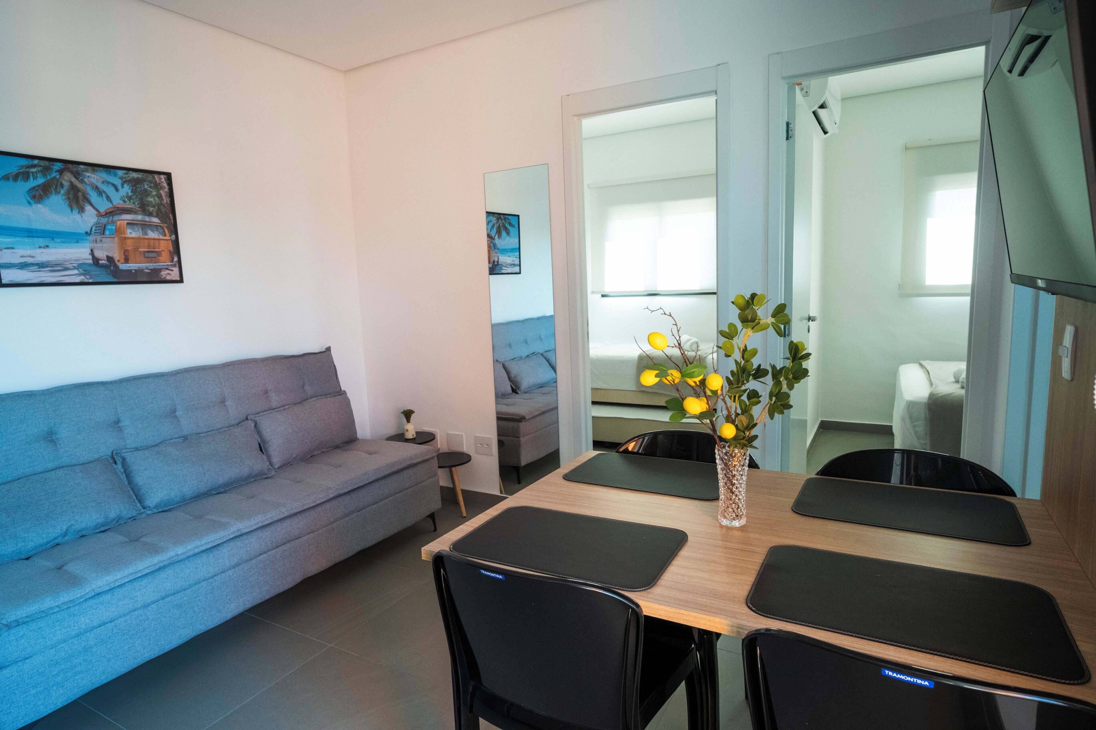 A modern living room with a grey sofa, a dining table with four chairs, and a small side table.