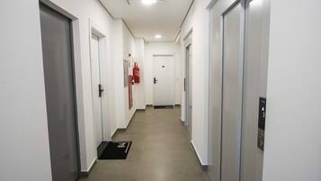 A corridor with doors on both sides, a fire extinguisher mounted on the wall, and a doormat at the entrance.