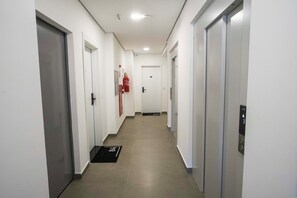 A corridor with doors on both sides, a fire extinguisher mounted on the wall, and a doormat at the entrance.