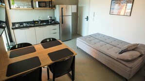 Un espacio habitable compacto con kitchenette, una mesa de comedor con cuatro sillas, un sofá con cojines y un cuadro en la pared.