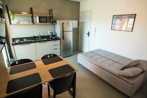Un espacio habitable compacto con kitchenette, una mesa de comedor con cuatro sillas, un sofá con cojines y un cuadro en la pared.