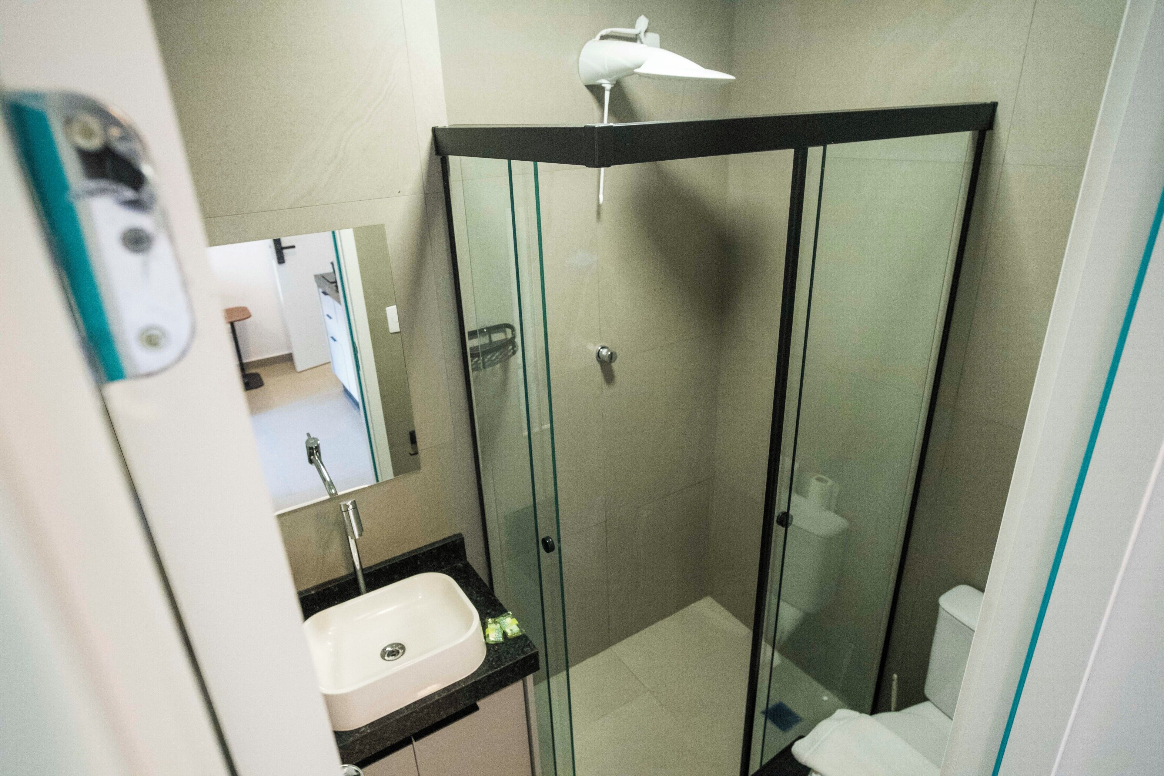 Casa de banho moderna com cabine de duche envidraçada, lavatório branco e espelho sobre o lavatório.