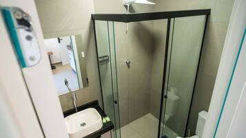 Casa de banho moderna com cabine de duche envidraçada, lavatório branco e espelho sobre o lavatório.
