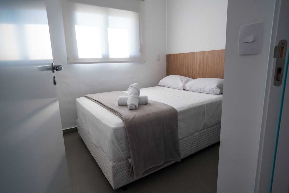 A single bed with a headboard, a window with blinds, and a door with a handle.