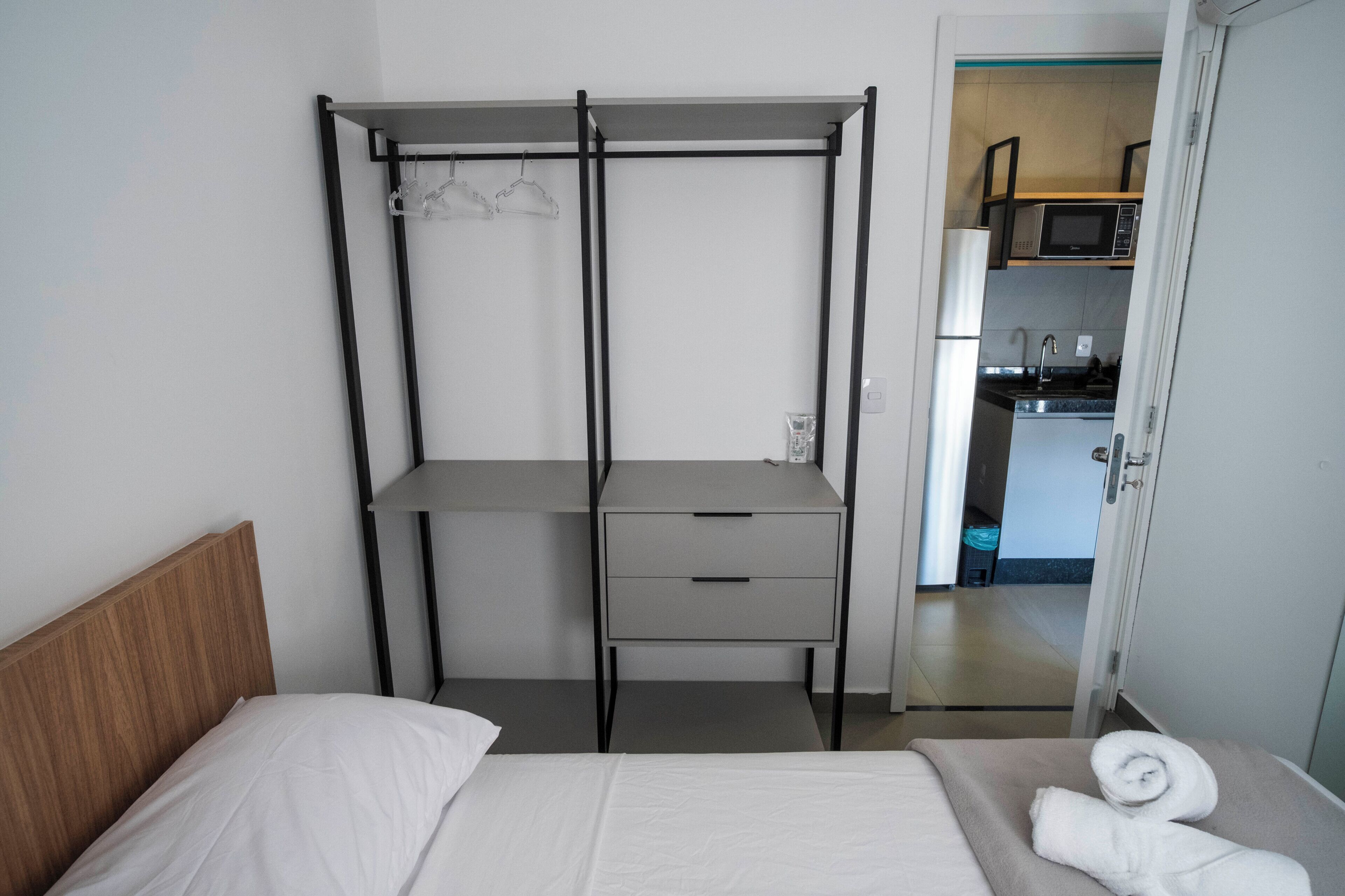 A bedroom with a bed, a bedside table, a wardrobe, and a view into the kitchen.