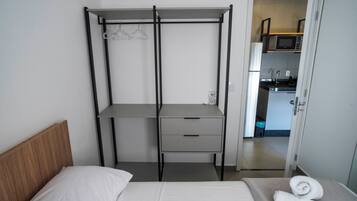 A bedroom with a bed, a bedside table, a wardrobe, and a view into the kitchen.