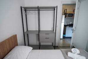 Un dormitorio con cama, mesita de noche, armario y vista a la cocina.