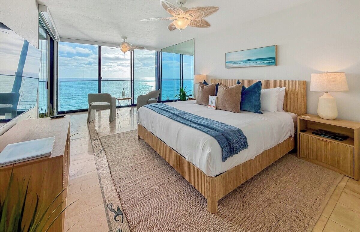 Un dormitorio moderno con una cama grande, un escritorio y una silla, con vistas a un paisaje marino.