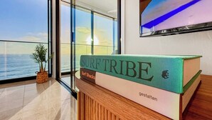 Ein Buch mit dem Titel 'SURF TRIBE' auf einer Holzauslage, mit Blick auf das Meer durch große Fenster.
