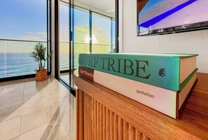 Ein Buch mit dem Titel 'SURF TRIBE' auf einer Holzauslage, mit Blick auf das Meer durch große Fenster.