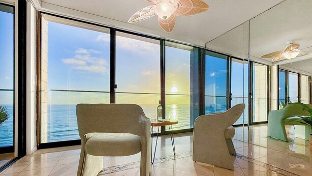 Ein modernes Interieur mit großen Fenstern, einem Deckenventilator und Meerblick.