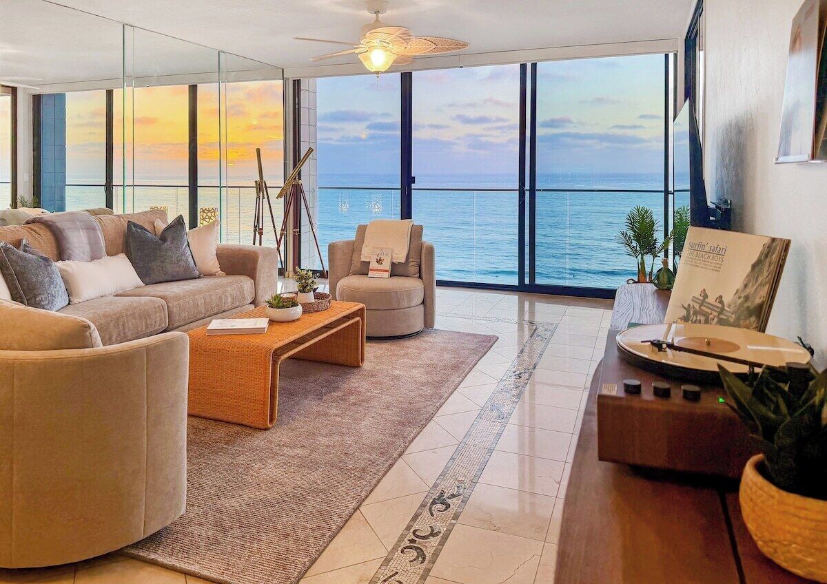 Ein modernes Wohnzimmer mit großem Fenster zum Meer, einer Sofagarnitur, einem Couchtisch und einem Plattenspieler.