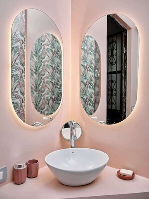 A bathroom with a white sink, two oval mirrors, and a floral wallpaper. - Charming Apartment in Milan (Milano)