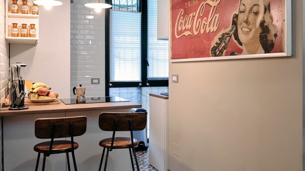 Et køkken med en bar, et Coca-Cola plakat og et vindue med persienner.