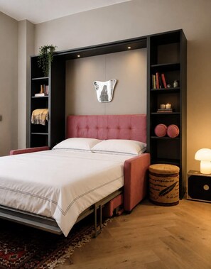 A modern bedroom with a tufted headboard, a bedside lamp, and a decorative mirror. - Charming Apartment in Milan (Milano)