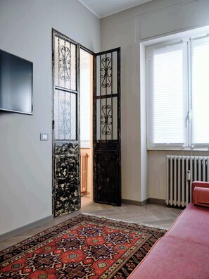 A room with a patterned carpet, a radiator, a window with blinds, and a closed door with decorative panels. - Charming Apartment in Milan (Milano)