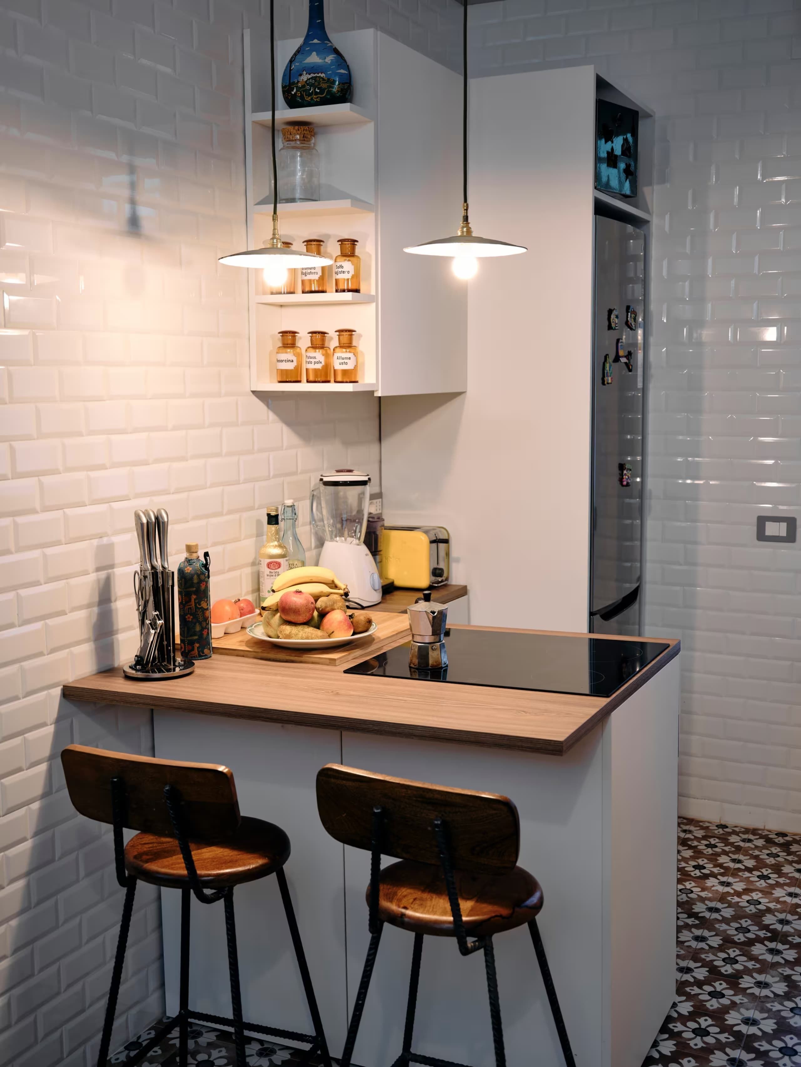 Een moderne keuken met een centraal eiland, twee barkrukken, hangende hanglampen en een witte bakstenen spatwand.