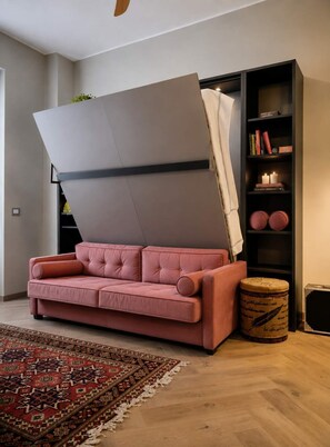 Ein Zimmer mit einer Schlafcouch, einem Bücherregal und einem dekorativen Teppich.