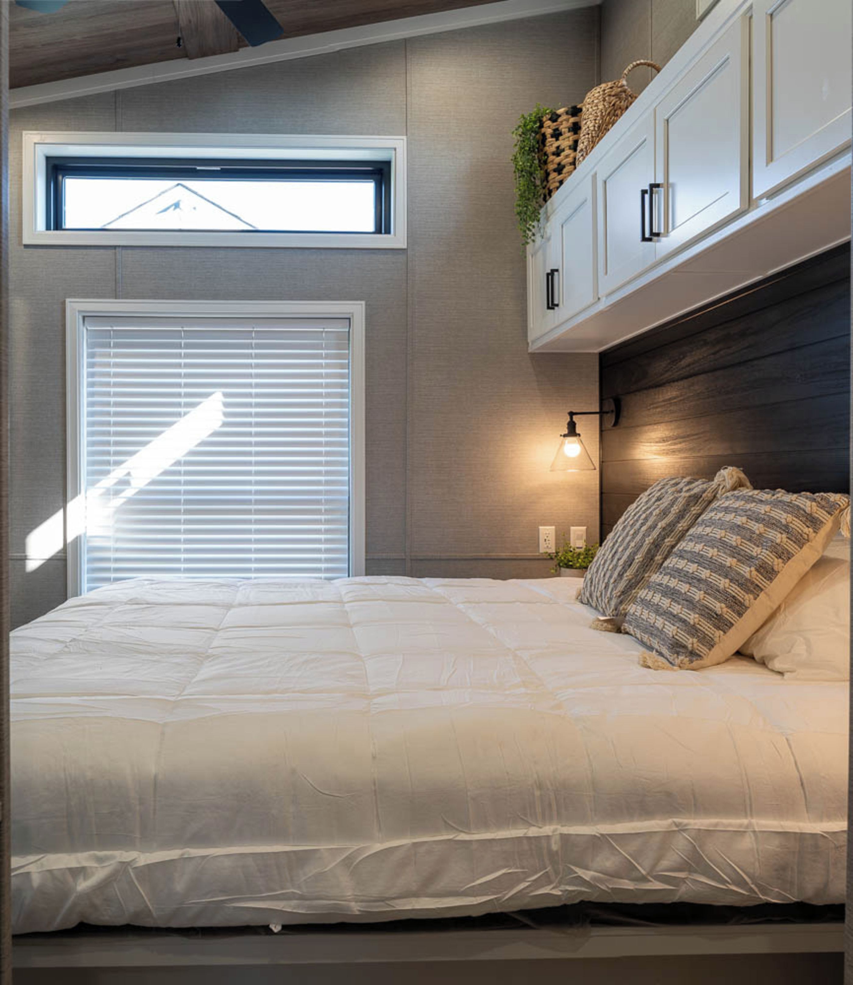 Een slaapkamer met een bed, een raam met jaloezieën, een wandlamp en een plafondventilator.