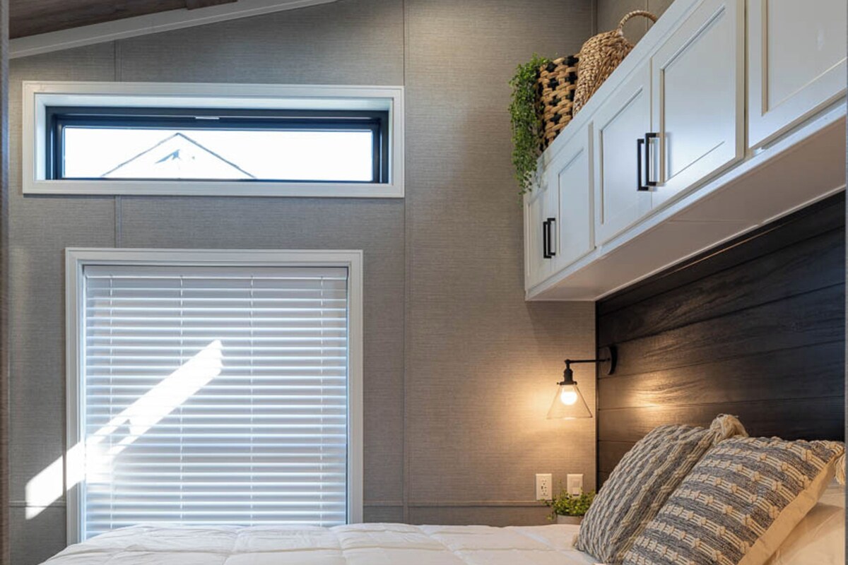 A bedroom with a bed, a window with blinds, a wall-mounted light, and a ceiling fan.