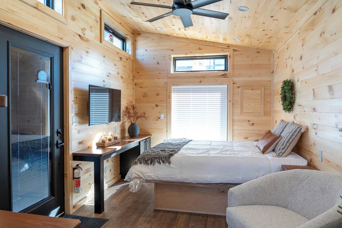 A bedroom with a bed, a desk, a chair, a ceiling fan, and a window.