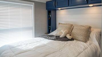 Un dormitorio con una cama, almohadas, un ventanal con persianas y armarios azules sobre la cama.