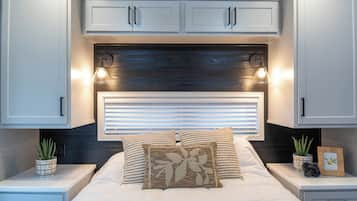 Un dormitorio con cama, dos mesitas de noche, cabecero con iluminación integrada y ventana con persianas.